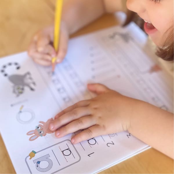 Child working on a worksheet with animal illustrations, holding a yellow pencil.