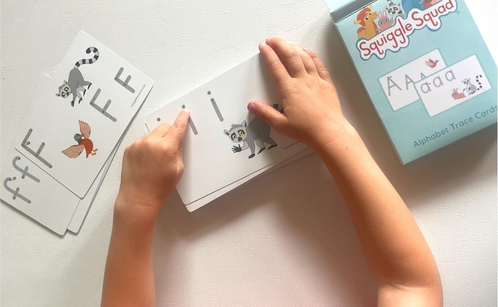 Child using alphabet trace cards with images of animals and letters.