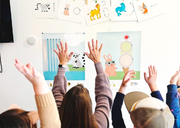 People raising their hands in front of illustrated animal posters on a wall.